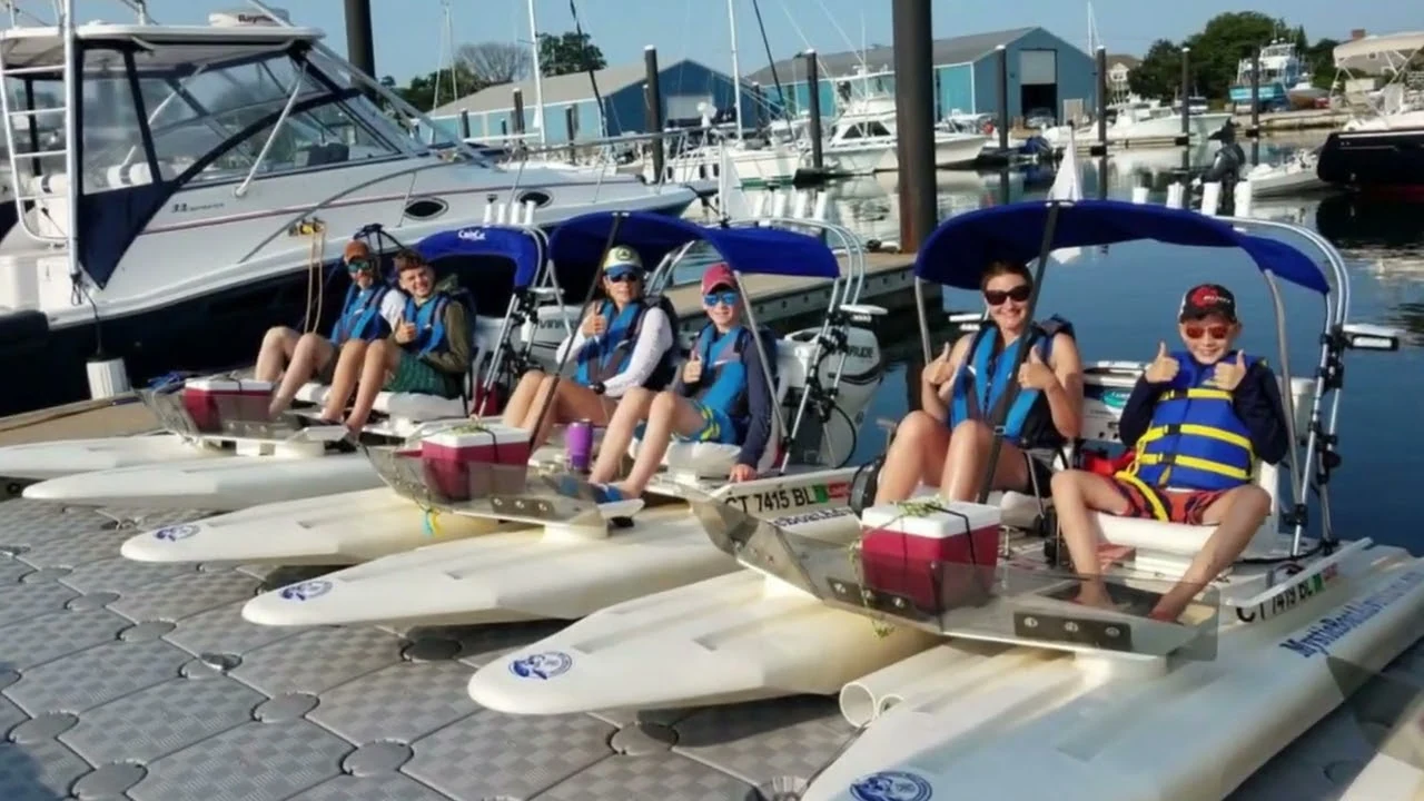 Guests seated in mini powerboats beside a Mystic-area marina dock