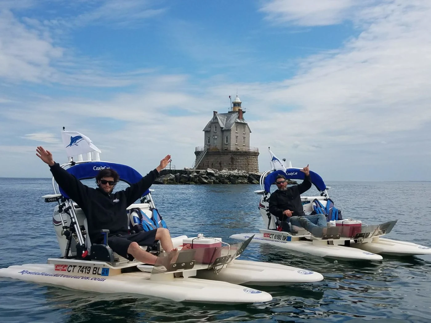 Guests driving separate mini powerboats across coastal water near a lighthouse